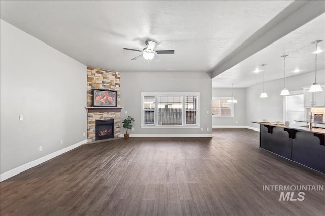 unfurnished living room featuring dark wood-type flooring, a fireplace, baseboards, and ceiling fan