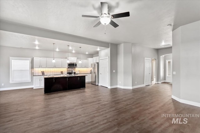 kitchen with dark wood-style floors, backsplash, appliances with stainless steel finishes, open floor plan, and white cabinetry