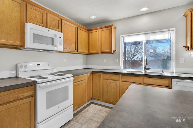 kitchen with dark countertops, light floors, white appliances, and a sink