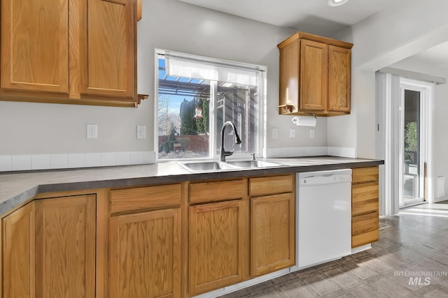 kitchen with dark countertops, light floors, brown cabinets, white dishwasher, and a sink