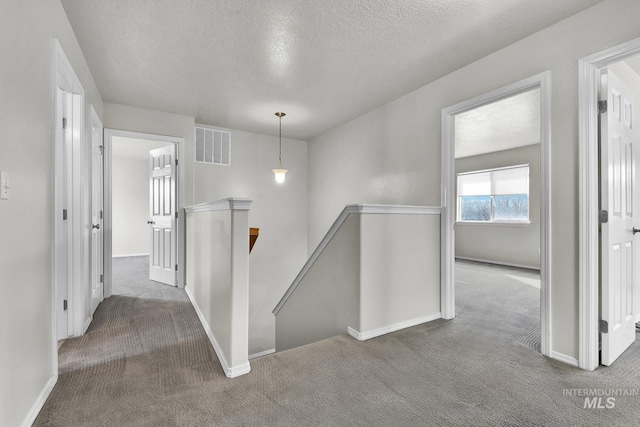 hallway featuring visible vents, baseboards, carpet floors, an upstairs landing, and a textured ceiling