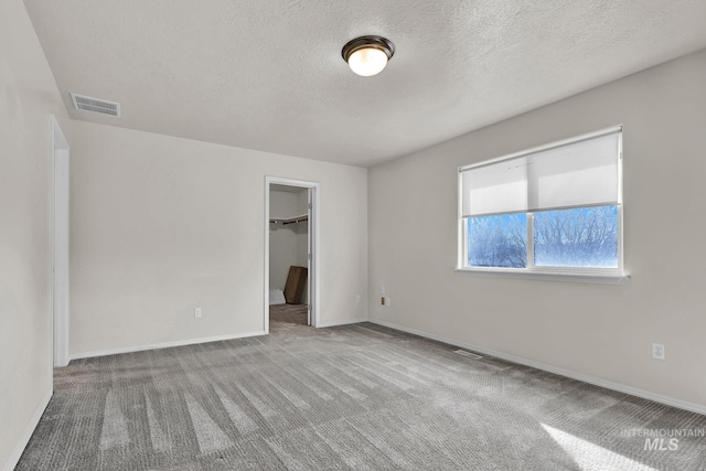 unfurnished bedroom featuring visible vents, a walk in closet, baseboards, carpet floors, and a textured ceiling