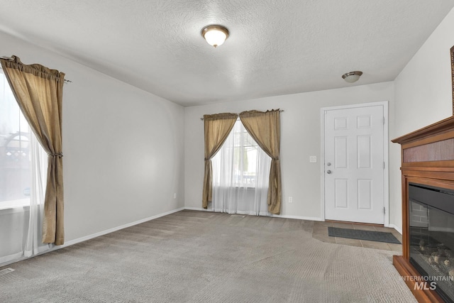 unfurnished living room with a glass covered fireplace, carpet, baseboards, and a textured ceiling