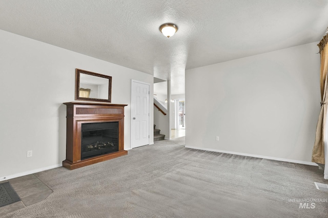 unfurnished living room with a textured ceiling, a glass covered fireplace, carpet flooring, baseboards, and stairs