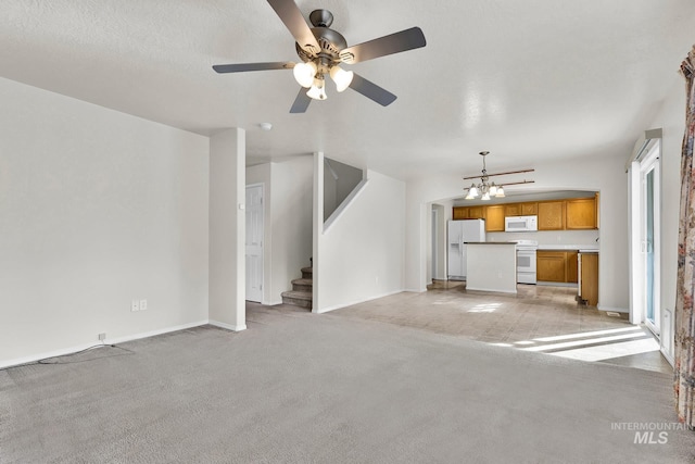 unfurnished living room with ceiling fan with notable chandelier, a textured ceiling, stairway, baseboards, and light colored carpet