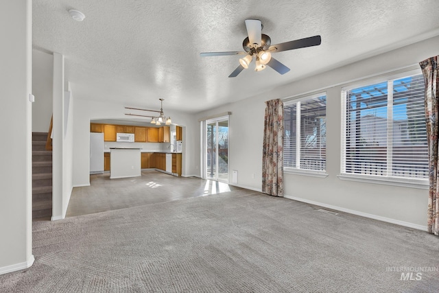 unfurnished living room featuring stairs, ceiling fan with notable chandelier, baseboards, and light carpet