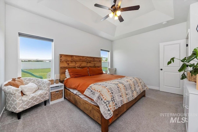 bedroom with ceiling fan, a raised ceiling, and light carpet