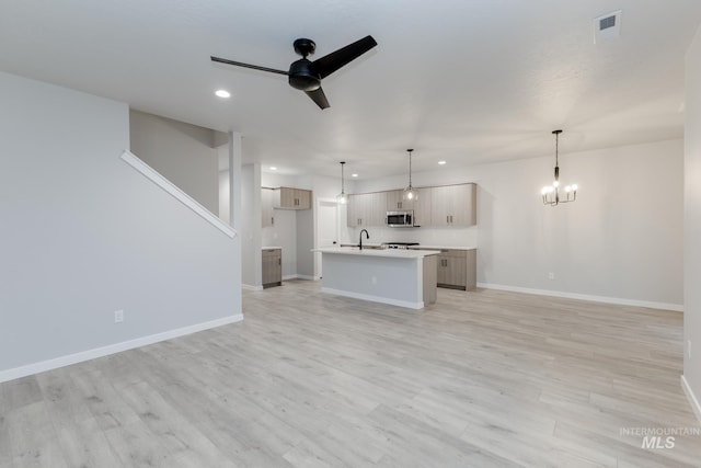 unfurnished living room featuring recessed lighting, ceiling fan with notable chandelier, a sink, baseboards, and light wood-type flooring