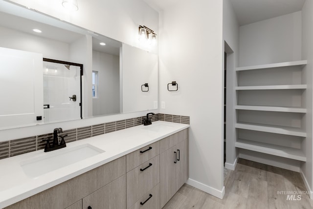 bathroom with double vanity, a shower stall, a sink, and wood finished floors