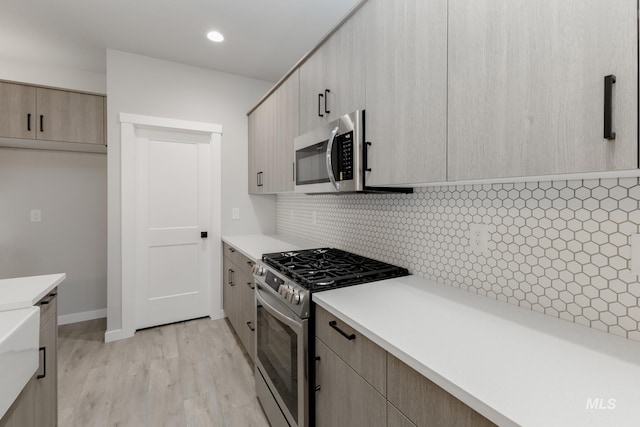 kitchen featuring stainless steel appliances, light wood-style floors, light countertops, backsplash, and modern cabinets