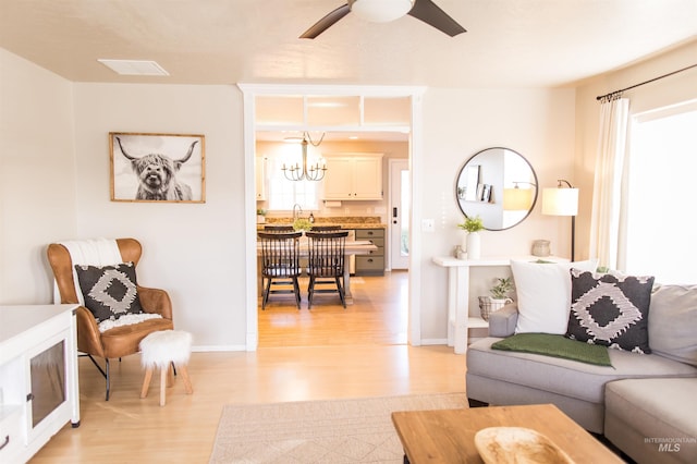 living room featuring a wealth of natural light, light hardwood / wood-style flooring, ceiling fan with notable chandelier, and sink