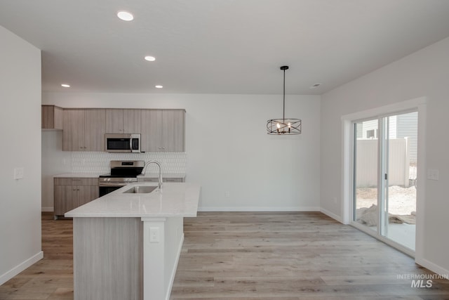 kitchen with light brown cabinets, a center island with sink, hanging light fixtures, appliances with stainless steel finishes, and sink