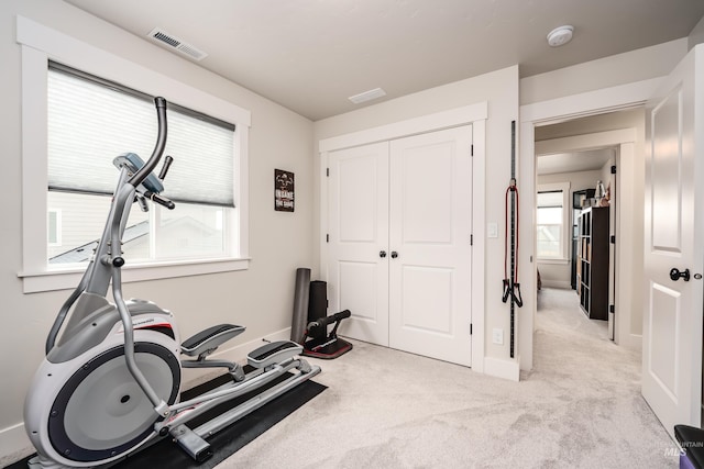 exercise room with visible vents, light colored carpet, and baseboards