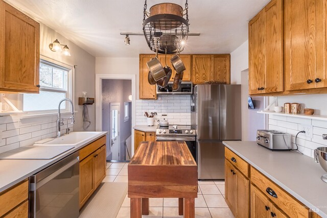 kitchen with light tile patterned floors, decorative backsplash, brown cabinets, stainless steel appliances, and a sink