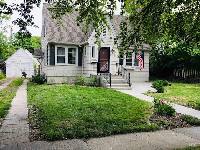 view of front facade featuring a front lawn, an outdoor structure, and roof with shingles