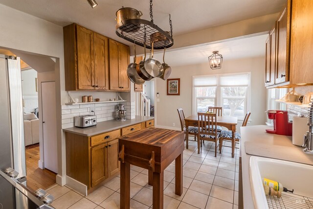 kitchen featuring baseboards, light countertops, light tile patterned floors, decorative backsplash, and brown cabinets