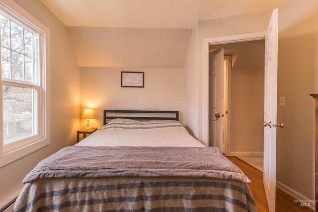 bedroom featuring wood finished floors, baseboards, and vaulted ceiling
