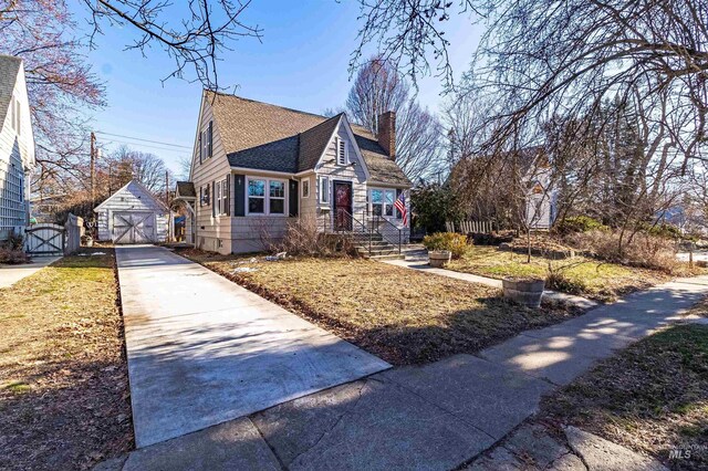 view of front facade featuring a shingled roof, concrete driveway, a chimney, a garage, and an outdoor structure