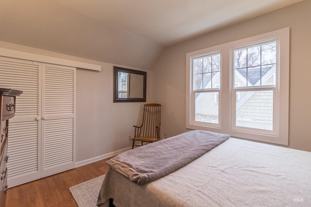 bedroom featuring a closet, vaulted ceiling, baseboards, and wood finished floors