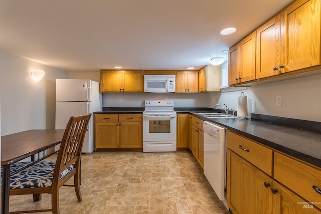 kitchen with white appliances, brown cabinetry, a sink, stone finish flooring, and dark countertops