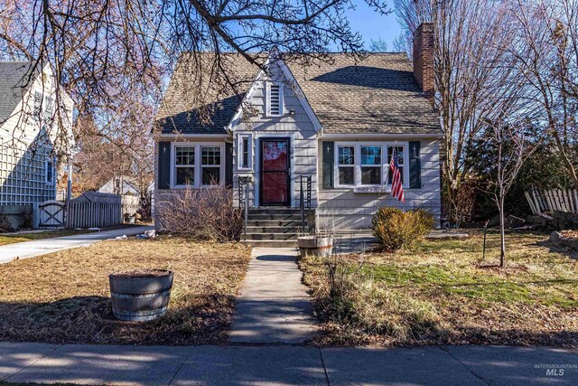 view of front of home with a chimney, roof with shingles, and fence