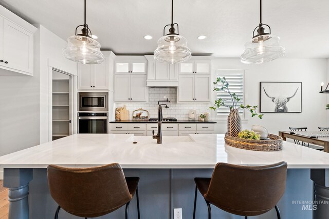 kitchen featuring white cabinets, stainless steel appliances, hanging light fixtures, and tasteful backsplash