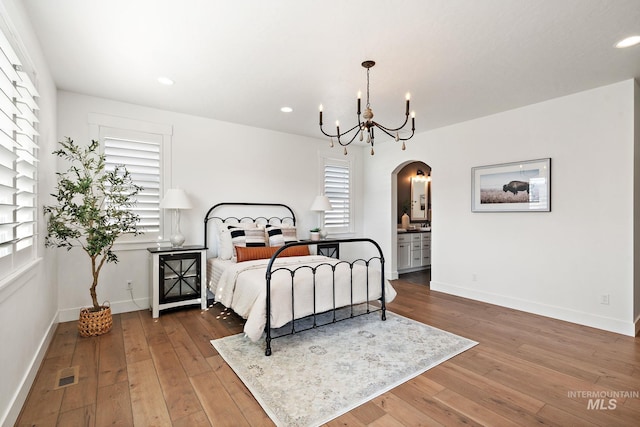 bedroom featuring an inviting chandelier, connected bathroom, and hardwood / wood-style floors