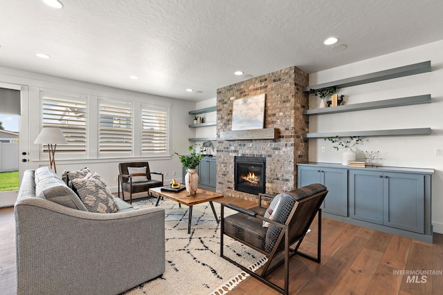 living room featuring a brick fireplace, a textured ceiling, and light wood-type flooring