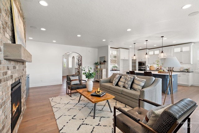 living room featuring a brick fireplace, a textured ceiling, and light wood-type flooring