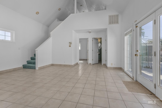 unfurnished living room with light tile patterned floors, baseboards, visible vents, stairway, and a high ceiling