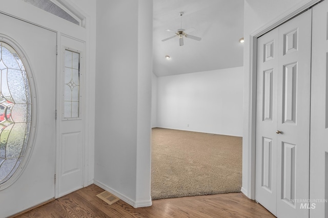 carpeted entrance foyer with lofted ceiling, a ceiling fan, visible vents, and wood finished floors