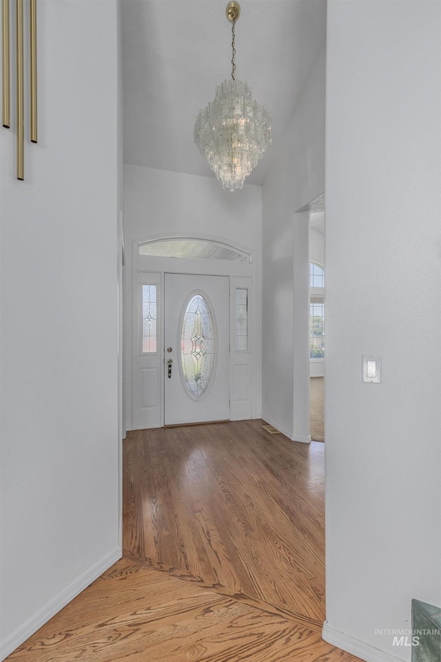 entryway with a wealth of natural light, a notable chandelier, baseboards, and wood finished floors