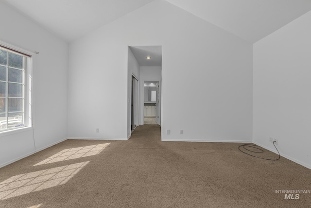 carpeted spare room with vaulted ceiling and baseboards