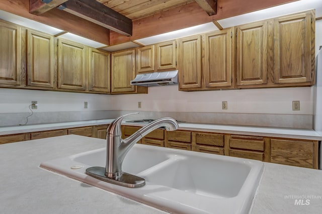 kitchen with beamed ceiling, light countertops, wood ceiling, under cabinet range hood, and a sink