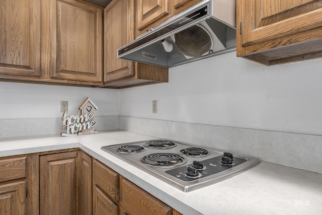 kitchen with light countertops, stainless steel stovetop, under cabinet range hood, and brown cabinets