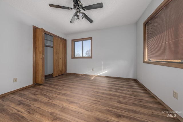 unfurnished bedroom with baseboards, a ceiling fan, dark wood finished floors, and a closet