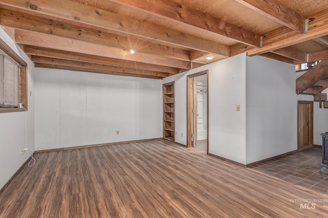 finished below grade area featuring baseboards, a wood stove, and wood finished floors