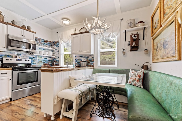 kitchen with appliances with stainless steel finishes, coffered ceiling, white cabinets, breakfast area, and decorative light fixtures