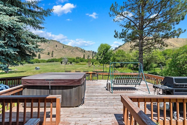 wooden terrace with a hot tub, a mountain view, area for grilling, and a yard