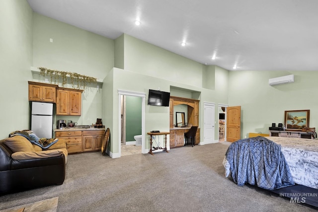 carpeted bedroom featuring white fridge, an AC wall unit, high vaulted ceiling, and ensuite bath