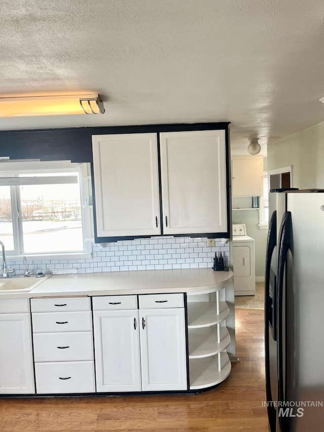 kitchen with fridge with ice dispenser, a sink, washer / dryer, backsplash, and white cabinetry