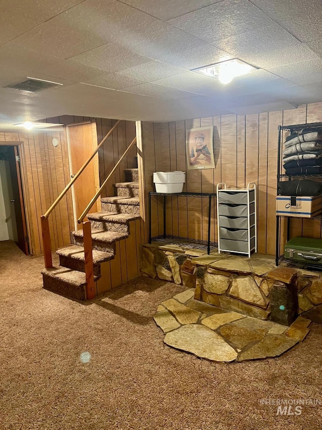 finished below grade area with visible vents, stairway, wooden walls, and carpet flooring