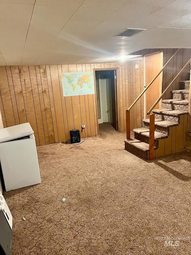 finished below grade area with wooden walls, visible vents, stairway, and carpet