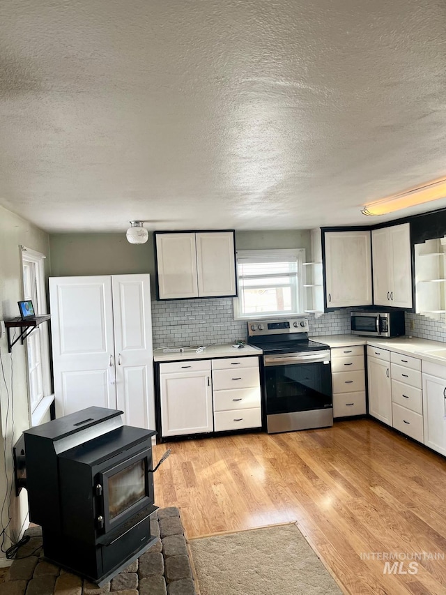 kitchen featuring light wood-style flooring, decorative backsplash, stainless steel appliances, light countertops, and a textured ceiling