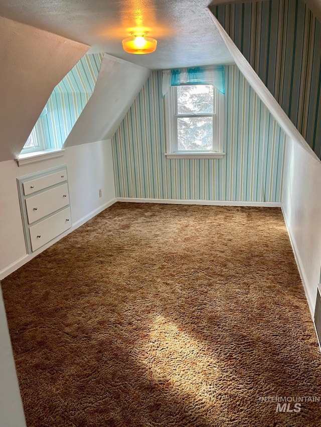 additional living space with wallpapered walls, vaulted ceiling, carpet floors, and baseboards