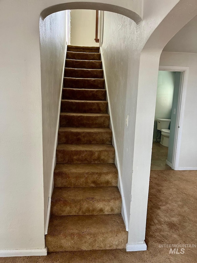 stairway featuring arched walkways, carpet, and baseboards
