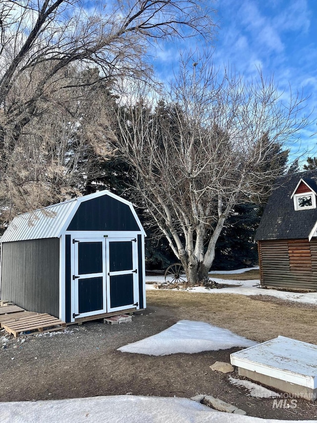 snow covered structure featuring an outdoor structure and a storage shed