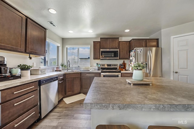 kitchen featuring appliances with stainless steel finishes, dark brown cabinets, a textured ceiling, sink, and hardwood / wood-style floors