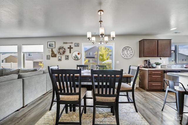 dining space featuring light hardwood / wood-style floors, a textured ceiling, and an inviting chandelier