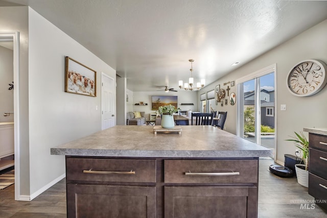 kitchen with pendant lighting, ceiling fan with notable chandelier, dark hardwood / wood-style floors, a kitchen island, and dark brown cabinetry